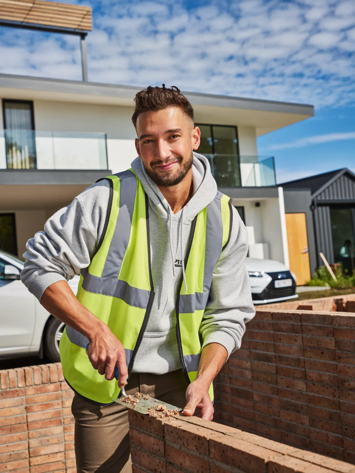 A builder in a hi-vis vest laying bricks on a new garden wall