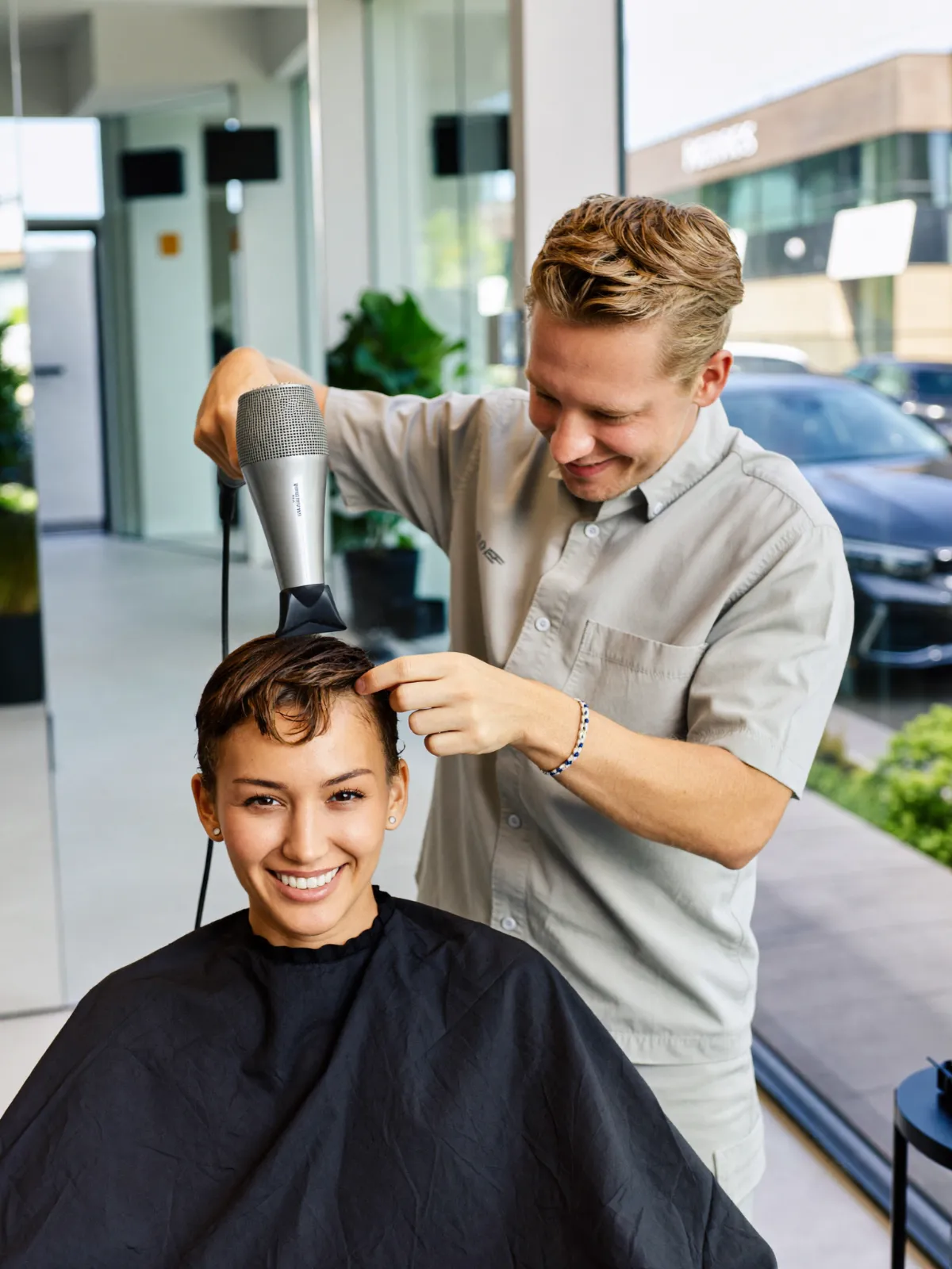 A hairdresser blow-drying a smiling client’s hair in a bright salon