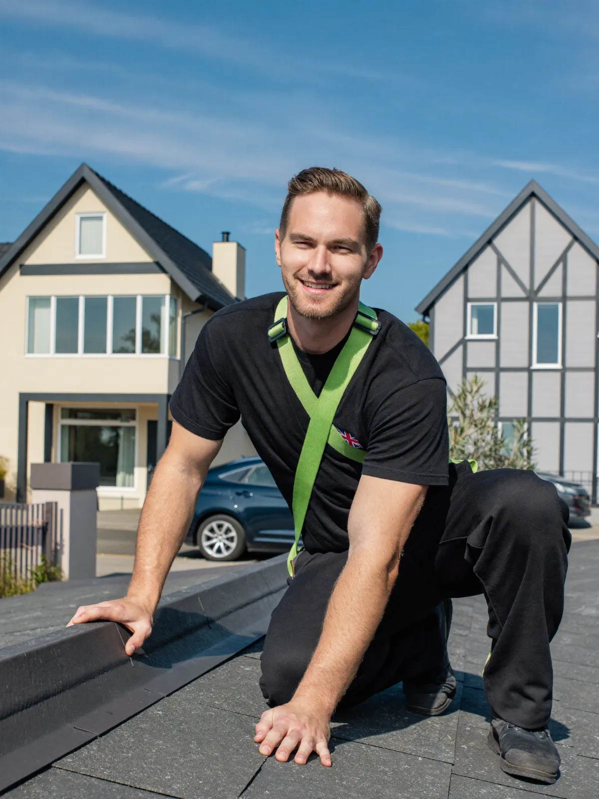 A roofer in a safety harness kneeling on a slate roof on a sunny day
